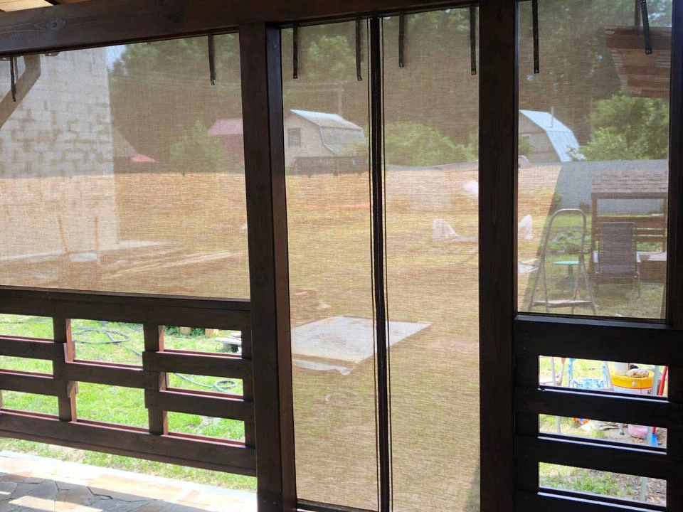 Вид изнутри беседки через бежевые защитные шторы